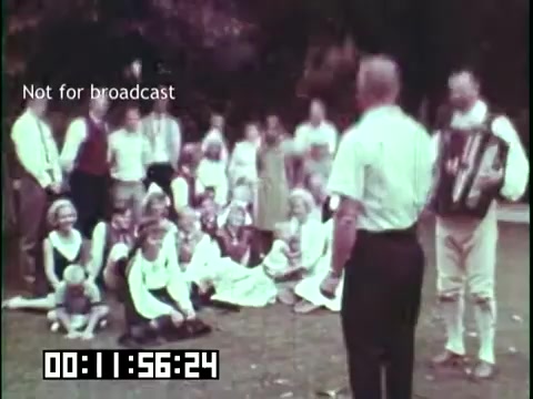 The still from 'Immigrant Heritage,' featuring the Irish Rovers, depicts a lively outdoor scene where a diverse audience gathers to watch a performance. A man plays the accordion, engaging the crowd, which includes children and adults sitting on the grass, captivated by the show. The overall atmosphere is festive and communal, highlighting themes of cultural celebration and heritage. The 'Not for broadcast' label suggests that this image is part of private archival material.