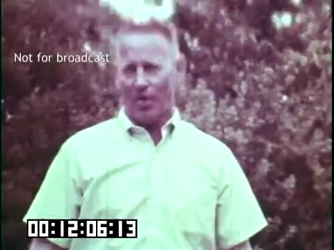 The still from 'Immigrant Heritage' features a man outdoors, speaking directly to the camera. He appears to be in casual attire, wearing a light-colored shirt. In the background, there is a blurred green landscape, suggesting a rural or natural setting. The image includes a time code and a note indicating it's not for broadcast, emphasizing its educational context related to immigrant heritage and the Irish Rovers.