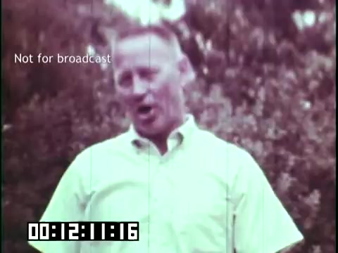 The still from 'Immigrant Heritage' features a middle-aged man speaking directly to the camera. He is wearing a light-colored button-down shirt and has a cheerful demeanor. The background appears lush, suggesting an outdoor setting. Superimposed text indicates that this footage is not for broadcast, and a timecode is visible at the bottom. The overall tone of the image suggests an educational focus on cultural heritage, likely related to Irish immigration.
