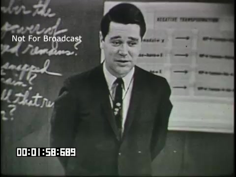 The still features a male educator in a suit, standing in front of a chalkboard with written notes and a poster displaying a chart labeled 'Relative Pronouns.' He appears to be engaging with an audience, possibly students, as part of an educational segment focused on linguistics for sixth graders. The overall tone seems instructional and informative.
