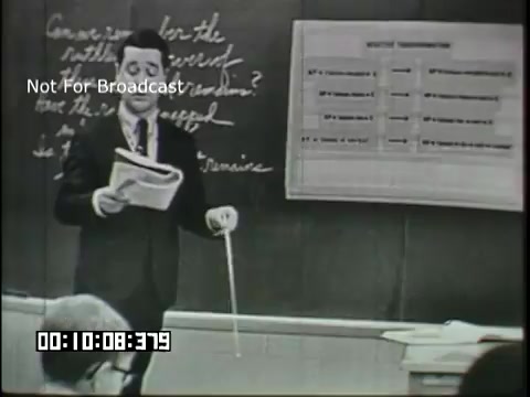 The still features a male teacher standing in front of a classroom blackboard, holding papers in one hand and a pointer in the other. The blackboard displays handwritten notes, possibly related to a linguistics lesson, and a chart on the right side. The teacher appears to be engaging with students, emphasizing a point in the lesson. The context suggests an educational setting focused on linguistic concepts aimed at sixth graders.