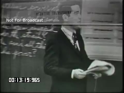 The still features a man, likely a teacher, standing in front of a blackboard. He is dressed in a suit and appears to be holding papers, possibly related to the lesson. The background displays handwritten notes or diagrams relevant to linguistics, reflecting an educational context aimed at sixth graders. The image conveys a formal classroom setting typical of a mid-20th-century educational film.