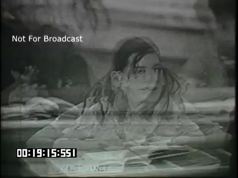 The still features a classroom setting from a 16mm educational film titled 'Sixth Grade Linguistics.' A student is depicted seated at a desk with papers in front, seemingly engaged in a lesson. The image has a slight overlay or blur, possibly indicating it captures a significant moment in the film, such as a discussion or explanation related to linguistics. The timecode and 'Not For Broadcast' label are also visible, indicating this is an archival or educational clip.