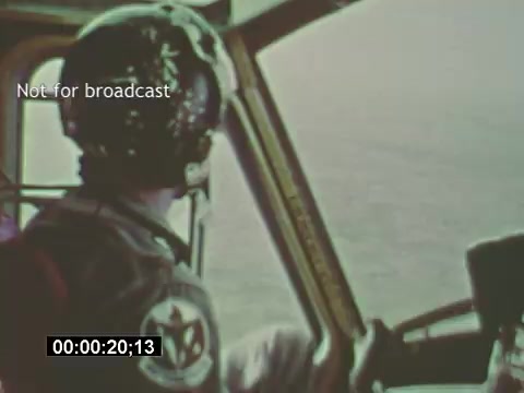 The 16mm still from 'USAF Helicopter Training footage - Bell UH-1 Huey' captures a pilot in the cockpit, wearing a helmet and headset, as he looks out over an expansive landscape. The shot emphasizes the operational perspective of the pilot while showcasing the interior of the helicopter. The footage is not intended for broadcast, suggesting it is part of training or internal documentation. The image conveys a sense of focus and professionalism typical in military aviation training.