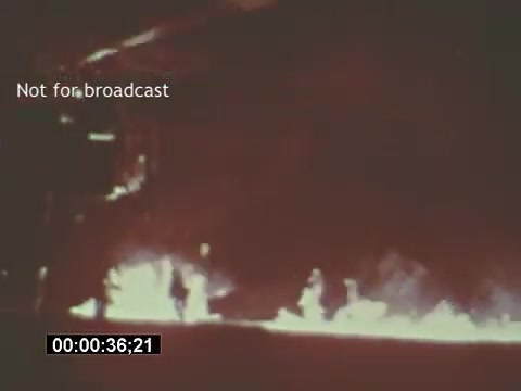 The still shows a dramatic scene from the USAF helicopter training footage, featuring flames in the foreground. The image suggests a training exercise, likely involving the Bell UH-1 Huey helicopter, with silhouettes of personnel visible against the backdrop of fire. The colors are muted, typical of 16mm film, conveying an intense atmosphere. Text indicates that the footage is not for broadcast.