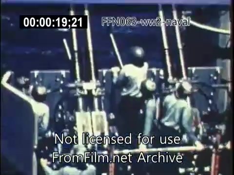 The still shows a scene from U.S. naval operations during World War II, focusing on a group of sailors on deck. They are likely engaged in preparations or responses to kamikaze attacks, highlighting the tense atmosphere of the time. The navy personnel are equipped with helmets and appear alert, ready for action amidst the backdrop of the ocean. The image captures the intensity and urgency of naval warfare during this historic period.