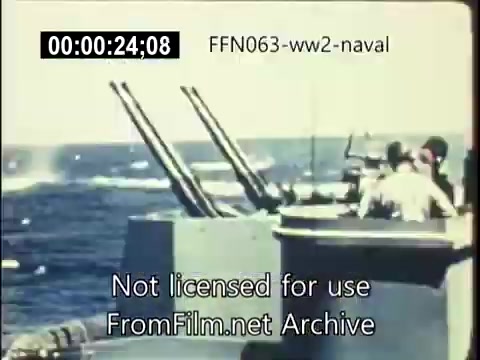 The still shows a naval ship during World War II, equipped with anti-aircraft guns facing the ocean. The crew is actively engaged, likely in response to incoming threats. The background illustrates a blue sea, revealing the intensity of combat operations against kamikaze attacks. The footage conveys the urgency and danger sailors faced during this period.