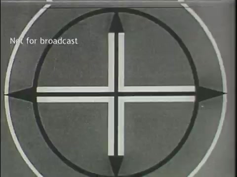 The still features a circular target graphic with a cross in the center, flanked by arrowheads pointing outward. The design is monochromatic, primarily in shades of gray and white, and includes a label stating 'Not for broadcast.' It serves as an intro or transition graphic typical in film footage, often used to denote the beginning of a segment or a point of focus.