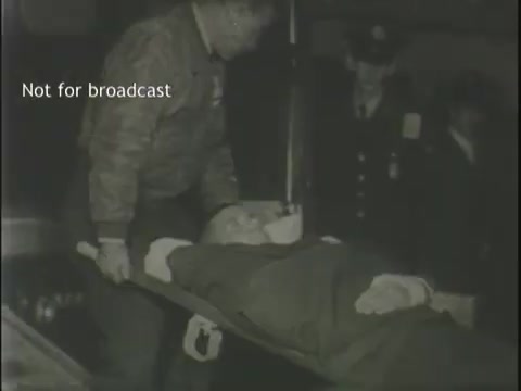 The still shows emergency responders carrying a stretcher with an individual, likely an injured or deceased person, in a somber setting. There are several figures in the background, possibly law enforcement or additional emergency personnel, observing the situation. The image conveys a serious and distressing moment, typical of news footage relating to accidents or emergencies. The watermark indicates that the footage is not for broadcast.