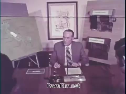 In the still from the 'Unleaded Gas Info' film segment, a man in a suit sits at a table, presenting information. Various charts and diagrams are displayed behind him, likely illustrating the benefits of unleaded gasoline. He highlights that vehicles using this fuel experience significantly longer lifespans for mufflers, exhaust pipes, and spark plugs, emphasizing the reduction of damaging acids and deposits. The setting suggests a formal presentation, aimed at informing the public or stakeholders about the advantages of unleaded fuel.