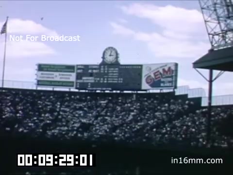 The 16mm still from the 'Briggs Stadium Detroit Tigers footage - 1948-1950' showcases a vibrant scene from a Tigers game during that era. The image features a scoreboard displaying game information, set against a backdrop of blue skies with fluffy clouds. The stadium is filled with spectators, indicating a lively atmosphere. A prominent clock is visible, emphasizing the time element of the event. This Kodachrome footage captures the essence of baseball culture in the late 1940s, making it a valuable historical record of the Detroit Tigers and their home ground.