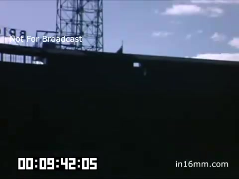 The 16mm still from 'Briggs Stadium Detroit Tigers footage - 1948-1950' captures a moment from a Tigers game during that era. The image shows the exterior of Briggs Stadium, featuring a shadowed facade against a backdrop of a blue sky with scattered clouds. A tower or structure is visible in the background, hinting at the stadium's design and atmosphere. The scene evokes a sense of nostalgia for mid-20th century baseball, showcasing a significant venue in the Tigers' history.