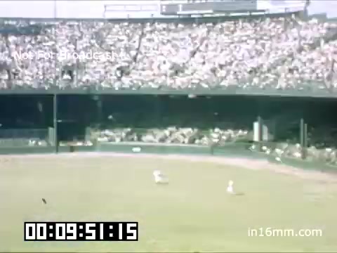 The still depicts a scene from a Detroit Tigers game at Briggs Stadium between 1948 and 1950. The stadium is filled with a large crowd, showcasing a vibrant atmosphere typical of baseball games during that era. Players can be seen on the field, engaged in play, while the colorful Kodachrome film captures the lively spirit of the event. The image likely reflects the classic design and structure of Briggs Stadium, contributing to the nostalgic feel of the footage.