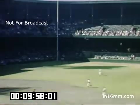 The still captures a scene from the 1948-1950 Detroit Tigers game at Briggs Stadium. The image shows a broad view of the baseball field, highlighting the stadium's structure and the outfield area. The stands are populated with spectators, reflecting the vibrant atmosphere of a mid-century baseball game. The color palette showcases the era's Kodachrome film typical of the time. It is labeled 'Not For Broadcast' and features a timestamp at the bottom, indicating a specific moment in the footage.