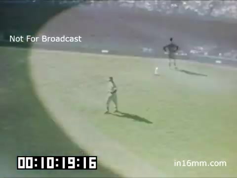 The still is from a 16mm Kodachrome footage of a Detroit Tigers game at Briggs Stadium, dating between 1948 and 1950. The scene shows a player in the outfield seemingly preparing for play, with a bright circular light illuminating part of the field. The background features stands filled with spectators, capturing the atmosphere of a mid-century baseball game. It's marked “Not For Broadcast,” indicating it's likely archival footage. The time code displays 00:10:19:16, suggesting it's from an early segment of the recording.