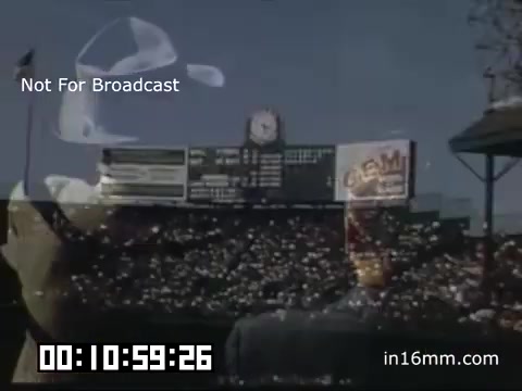 The still captures a moment from a Detroit Tigers game at Briggs Stadium between 1948 and 1950. The image showcases the iconic stadium's notable features, including a scoreboard displaying game details and a large crowd of fans in the stands. The presence of flags suggests a lively atmosphere, and the vintage Kodachrome film gives the scene a vibrant, nostalgic quality. The timestamp indicates ongoing footage, emphasizing the dynamic nature of the game day experience during this era. The watermark notes that the image is not for broadcast.