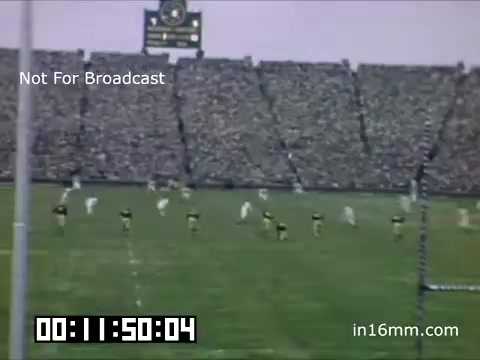 The still features a football game from the University of Michigan Wolverines, captured in the late 1940s to 1950. The stadium is filled with spectators, and players are seen on the field, ready for action. In the background, a scoreboard displays information, while a timestamp at the bottom indicates non-broadcast use. The color tone suggests it was filmed in early color film technology.