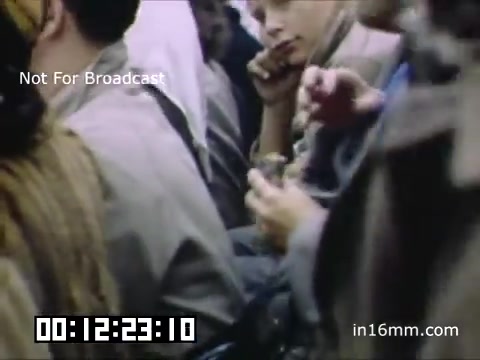 The still depicts a crowded scene likely from a parade or festive gathering associated with the University of Michigan Wolverines in the late 1940s to early 1950s. Participants appear engaged, wearing typical attire of the era, and are arranged in close proximity, suggesting a lively and communal atmosphere. The color tone reflects the period's film quality, likely giving a nostalgic feel. The overlay indicates that the footage is not for broadcast, and a timer is displayed at the bottom.