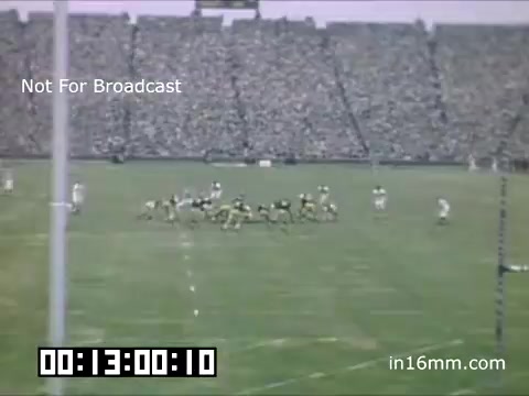 The still captures a moment from a 16mm film depicting a University of Michigan Wolverines football game between 1948 and 1950. The scene shows a lively stadium filled with spectators, highlighting the energy of American football during that era. The teams are positioned on the field, with players in yellow and blue uniforms, indicative of the Wolverines' colors. The atmosphere suggests a vibrant and competitive sporting event, reflective of college football culture in mid-20th century America.