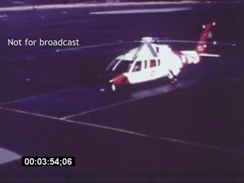 The still from the 'Sikorski S-76 Promotional Film' shows a Sikorski S-76 helicopter on a tarmac. The helicopter features a distinctive design with a white body and red accents, parked with its rotors stationary. The image also includes a timestamp indicating the point in the film, and a text overlay stating 'Not for broadcast.' The overall appearance is typical of vintage promotional materials, showcasing the helicopter in a professional context.