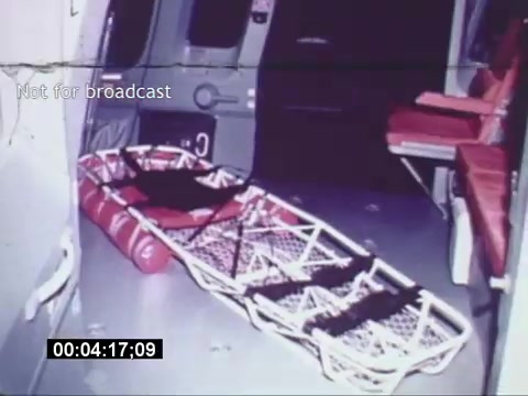 The still from the *Sikorski S-76 Promotional Film* shows the interior of the helicopter, highlighting the spacious cabin. A stretcher is positioned prominently, suggesting its use for medical emergencies or rescue operations. Red seating can be seen along one side, emphasizing the multifunctional design of the S-76. The frame also displays a timestamp and a note indicating the clip is not for broadcast. Overall, the image conveys the helicopter's capability for both passenger transport and medical support.