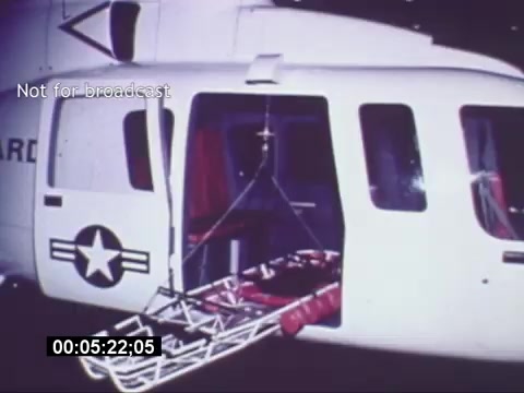 The still from the Sikorski S-76 promotional film depicts a helicopter with an open side door. Inside, a gurney is seen hanging, likely for medical use, highlighting the aircraft's capabilities in emergency medical situations. The presence of a military star insignia suggests its potential use in defense or rescue operations. The image captures a moment emphasizing the versatility and practicality of the Sikorski S-76 in critical scenarios.