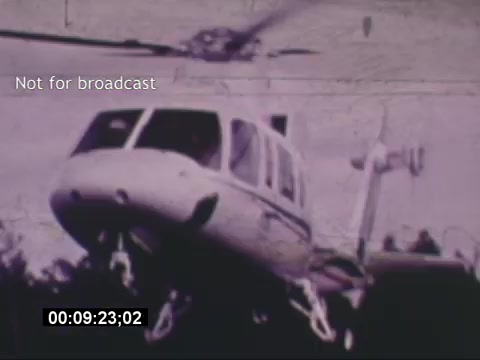 The still from the 'Sikorski S-76 Promotional Film' showcases a Sikorski S-76 helicopter in action. The image is visually focused on the aircraft, highlighting its sleek design and unique features. The helicopter appears to be taking off, with its rotors in motion, suggesting a dynamic scene. The background is somewhat blurred, emphasizing the helicopter as the focal point. Additionally, there’s a watermark stating “Not for broadcast” and a timestamp indicating the specific moment in the film. The overall aesthetic reflects the vintage quality of the 16mm film format.
