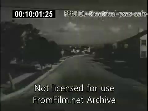 The still is from a 16mm film of a 1949 theatrical public service announcement focused on safe driving. It depicts a quiet suburban road, lined with trees and houses, conveying a sense of calm. The black-and-white imagery suggests a nostalgic or historical context, emphasizing the importance of road safety in a time when automobile use was becoming more widespread. The overlay text indicates the source and usage conditions of the content.