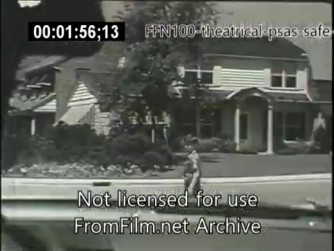 The still from the 1949 theatrical public service announcements focuses on safe driving. It features a suburban setting with a young child walking on the sidewalk near houses, highlighting the importance of vigilance and caution in residential areas. The visuals aim to promote awareness of pedestrian safety.