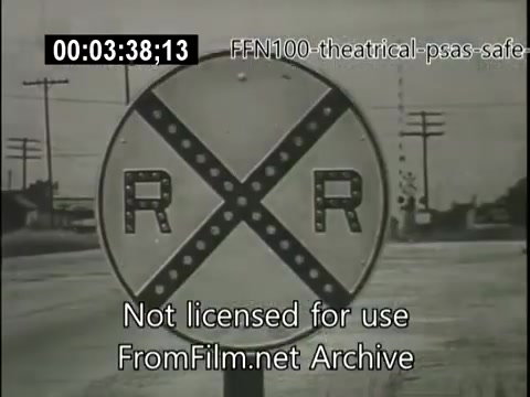 The still features a railroad crossing sign marked 'RR,' indicating a railway intersection. It is part of a 1949 theatrical public service announcement aimed at promoting safe driving. The background shows a road and utility poles, illustrating the transport context in which caution is needed. The overall tone conveys the importance of being aware of railroad crossings to prevent accidents.