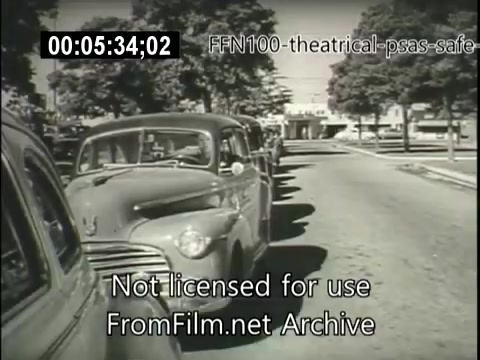 The still features a black-and-white scene from a 1949 public service announcement for safe driving. It shows several parked cars along a tree-lined street, emphasizing the importance of road safety. The scene appears to capture a moment typical of mid-20th-century America, focusing on the surrounding environment rather than specific events or actions. The text overlay indicates it is part of the FFN100 series and not licensed for use.