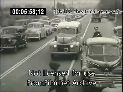 The still from the 1949 theatrical public service announcements for safe driving shows a busy street scene with several old cars, typical of the era. A police officer is present, possibly monitoring traffic or directing pedestrians. The image captures the vintage aesthetic and emphasizes themes of road safety, promoting awareness for safer driving practices in the post-war period.