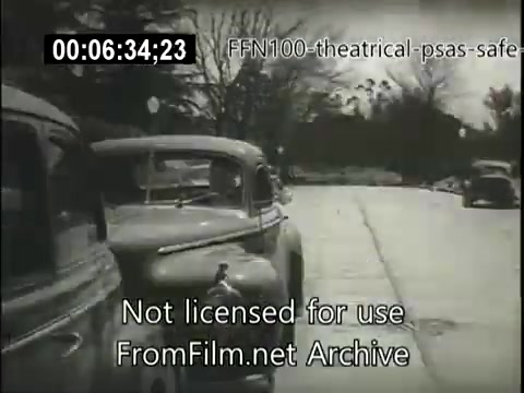 The still depicts a 16mm film from a 1949 public service announcement promoting safe driving. It shows a street scene with parked cars on the side, potentially illustrating the importance of caution and awareness on the road. The black-and-white image emphasizes the era's vintage aesthetic, aiming to convey a message about road safety during that time.