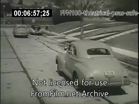 The still from the 1949 theatrical public service announcements for safe driving depicts several vintage cars parked along a suburban street. The scene suggests a quiet neighborhood environment, possibly aiming to promote safe driving behavior in residential areas. The cars, reflective of the era, hint at the mid-20th-century American automobile culture. The overall focus appears to be on raising awareness about safety on the roads.