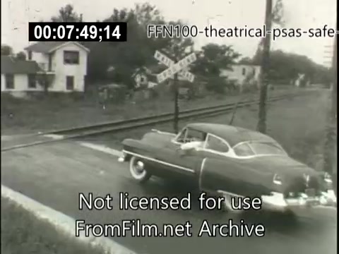 The still depicts a classic 1940s car approaching a railroad crossing, emphasizing safe driving practices. The scene is set in a rural area, with a house visible in the background and a railroad sign indicating caution. The image conveys a message about the importance of being vigilant and cautious near railway tracks, typical of public service announcements from that era promoting road safety.