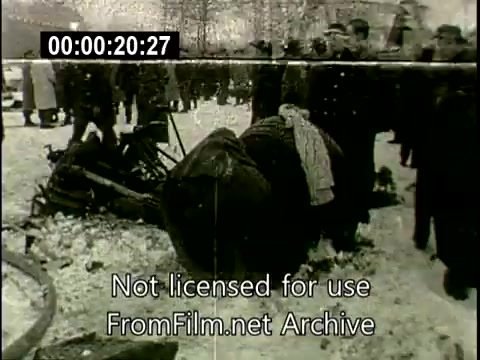 The still captures the aftermath of the December 16th, 1960, Staten Island plane crash involving the Lockheed Constellation N6907C. In the foreground, there is debris from the crash, partially covered in snow. A figure, possibly an investigator or official, is crouched near the wreckage, emphasizing the tragic scene. In the background, a crowd of onlookers, including uniformed personnel, observes from a distance, highlighting the gravity of the situation. The image conveys a somber atmosphere, reflecting the impact of the disaster.