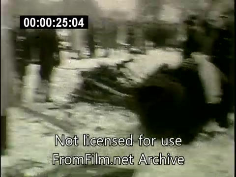 The still captures a chaotic scene from the aftermath of the Staten Island plane crash on December 16th, 1960, involving the Lockheed Constellation (N6907C) and a DC aircraft. In the image, debris is scattered across a snowy area, with a group of people, likely emergency responders and onlookers, gathered around the wreckage. The stark winter landscape adds to the somber atmosphere of the disaster's aftermath. The lower part of the frame includes a watermark indicating it's not licensed for use, sourced from the FromFilm.net Archive.