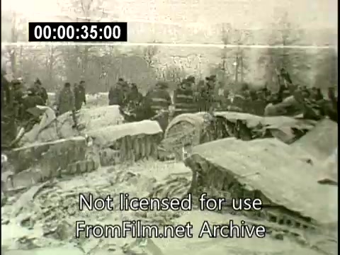 The still depicts the aftermath of the December 16, 1960, Staten Island plane crash involving the Lockheed Constellation N6907C. The scene is somber, featuring wreckage scattered across a snowy landscape, with a group of onlookers or emergency personnel gathered at the crash site. The environment appears bleak and cold, reflecting the tragic circumstances surrounding the incident. The visual conveys a sense of devastation and the urgency of the response to the disaster, typical of footage from that era.