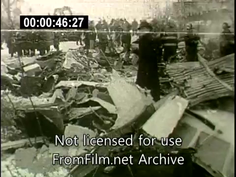 The still depicts the aftermath of the Staten Island plane crash that occurred on December 16, 1960. The image shows a chaotic scene of wreckage from the Lockheed Constellation and the DC aircraft, with fragmented debris scattered across the ground. First responders and onlookers are present, examining the site amidst the destruction, highlighting the tragic impact of the collision. The overall tone is somber, reflecting the seriousness of the incident.