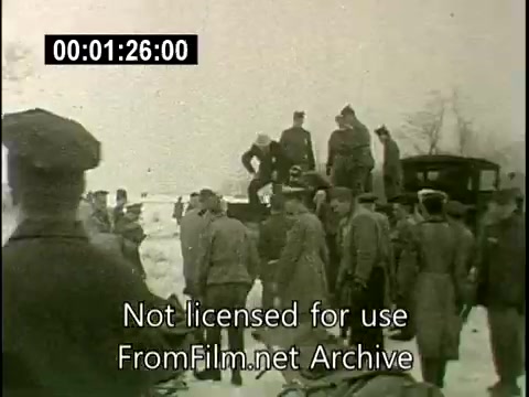 The still depicts a chaotic scene following the crash of the N6907C Lockheed Constellation in Staten Island on December 16, 1960. Various individuals, likely including first responders and onlookers, are gathered, some standing on a vehicle while others navigate the snowy ground nearby. The somber atmosphere underscores the aftermath of the mid-air collision, highlighting the seriousness of the incident. The footage appears to be historical news coverage, emphasizing the gravity and impact of the disaster.