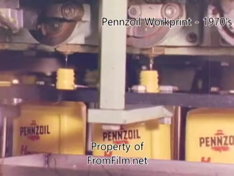 The still from the 'Pennzoil Factory⧸Refinery Workprint - 1980s' depicts a manufacturing environment where yellow Pennzoil containers are being filled. The machinery above seems to be dispensing the contents into the containers, indicative of an industrial setting. The overall aesthetic is characteristic of 16mm film from that era, featuring some visible debris in the film gate, which tends to occur with older film prints. The workprint likely showcases the processes involved in oil production or packaging at the refinery. The accompanying music by Underbelly adds a modern auditory layer to this historical footage.