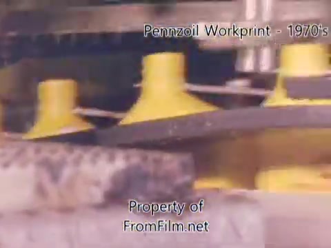 The still from the 'Pennzoil Factory/Refinery Workprint' features industrial machinery with prominent yellow components. The image captures a moment within the refinery setting, showcasing the equipment in operation. The subtle presence of debris in the film gate suggests the wear and age of the 16mm negative. Accompanied by music from Underbelly, the atmosphere evokes a sense of both industry and nostalgia.