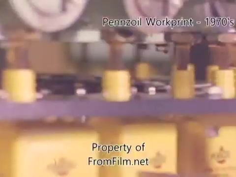 The 16mm still depicts an industrial scene from the Pennzoil refinery, showcasing machinery with yellow and metallic components. The film gate contains some visible debris, which may occasionally obscure the image. This workprint, originating from the 1980s, features accompanying music tracks by Underbelly, including 'I Hear Voices,' 'Asterism,' 'Italy Jr.,' and 'Land's End.' The overall aesthetic reflects a vintage, mechanical atmosphere characteristic of refinery operations.