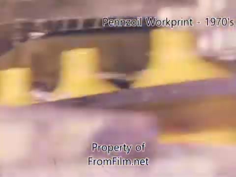 The 16mm still from the 'Pennzoil Factory⧸Refinery Workprint' showcases an industrial scene, likely featuring machinery and equipment typical of refinery operations. The image displays notable colorizations, with yellow elements prominent against a blurred background. There is visible debris in the film gate, indicative of its age. The accompanying music by Underbelly, including tracks like 'I Hear Voices' and 'Asterism,' adds an atmospheric layer to the visual narrative.