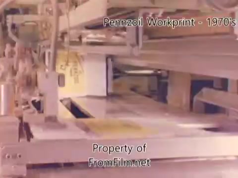The still from the 'Pennzoil Factory/Refinery Workprint - 1980s' features machinery in a refinery setting, showcasing the industrial processes involved in oil production. The image highlights the mechanical components and operations typical of a factory environment. There are visible signs of debris in the film gate, suggesting some wear or age in the footage. The accompanying music includes tracks from Underbelly, enhancing the atmosphere of the visuals.
