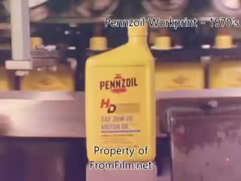The still features a close-up of a bright yellow Pennzoil motor oil bottle, prominently displaying the brand name and product details. Behind it, various yellow bottles are partially visible, suggesting a factory setting. The image is a frame from a 16mm workprint from the 1980s, likely documenting refinery processes. Notable is the presence of some film debris in the gate, which highlights its archival condition. The accompanying music is by Underbelly, with tracks that set an atmospheric tone.