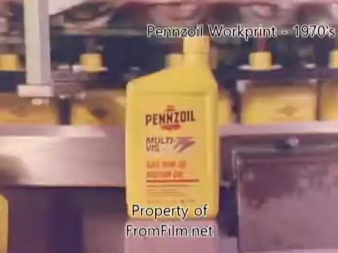 The still from the 'Pennzoil Factory⧸Refinery Workprint - 1980's' shows a close-up of a bright yellow Pennzoil oil bottle prominently displayed on a production line. The background features additional bottles and machinery typical of a refinery setting. The image likely captures the essence of 1970s industrial production, highlighting the branded packaging of Pennzoil motor oil. The film includes some noticeable debris in the film gate, contributing to the vintage aesthetic. The accompanying music by Underbelly adds a modern touch to the historical visuals.