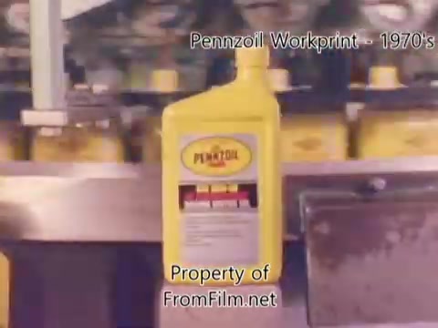 The 16mm still from the 'Pennzoil Factory/Refinery Workprint - 1980's' shows a close-up of yellow Pennzoil oil bottles on an assembly line. The labels are prominently displayed, highlighting the brand. The image reflects the industrial setting of a refinery, with some visible debris in the film gate, typical of workprint materials. The accompanying music from Underbelly enhances the atmosphere, offering a nostalgic and rhythmic backdrop to the visual of the production process.