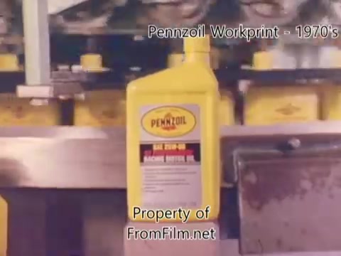 The still from 'Pennzoil Factory⧸Refinery Workprint - 1980's' showcases a production scene featuring yellow Pennzoil oil bottles on a conveyor system. The bottles are prominently displayed, highlighting the iconic brand. The film, shot on 16mm, shows some debris in the film gate, indicative of its workprint status. The soundtrack features tracks by Underbelly from the YouTube Audio Library, adding an atmospheric background to the visual content.