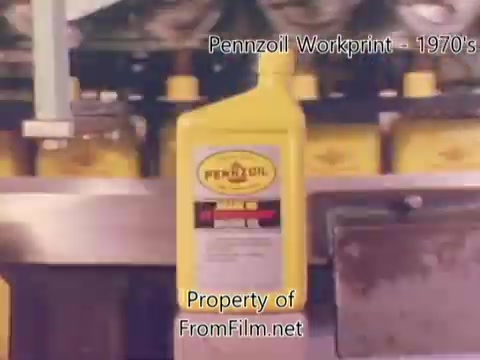 The still from the 'Pennzoil Factory/Refinery Workprint - 1980's' showcases a production line featuring yellow Pennzoil bottles. The film is derived from a 16mm negative and exhibits some debris in the film gate. The visual is accompanied by music from Underbelly, enhancing the industrial atmosphere of the refinery setting.